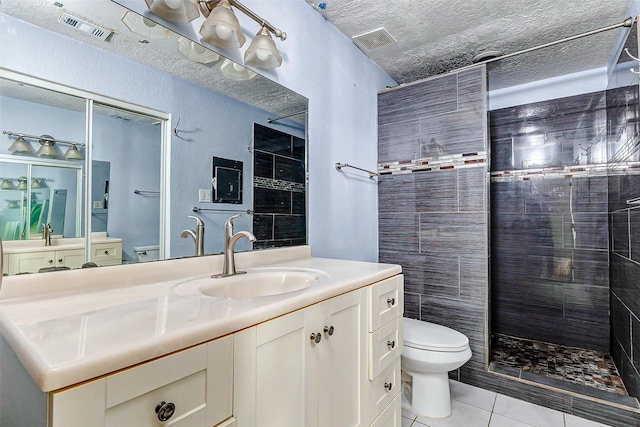 bathroom with a tile shower, vanity, toilet, tile patterned floors, and a textured ceiling