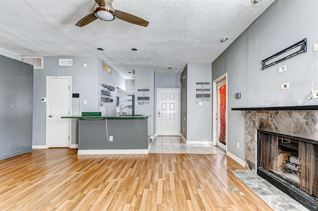 unfurnished living room featuring sink, ceiling fan, a fireplace, light hardwood / wood-style floors, and a textured ceiling