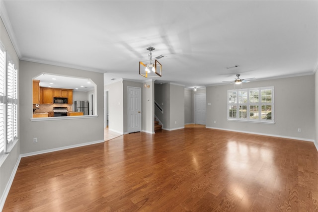 unfurnished living room with ceiling fan with notable chandelier, ornamental molding, and hardwood / wood-style floors