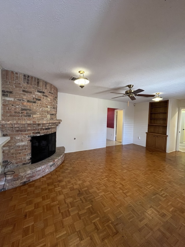 unfurnished living room featuring a brick fireplace, dark parquet floors, a textured ceiling, and ceiling fan