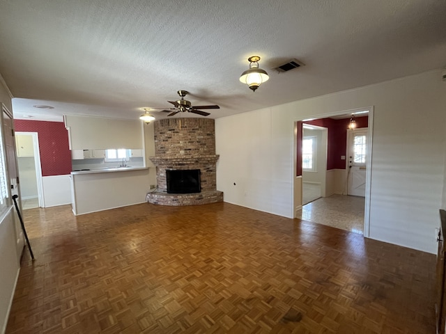 unfurnished living room with a brick fireplace, parquet floors, a textured ceiling, and ceiling fan