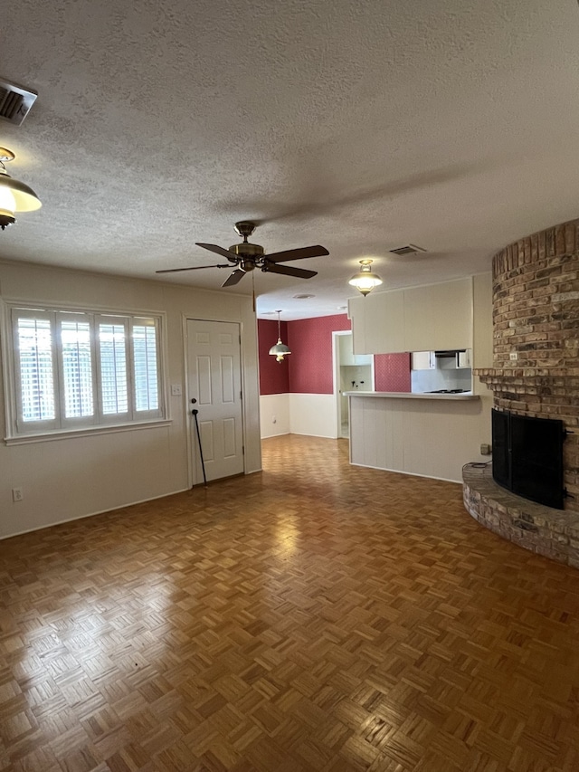 unfurnished living room with dark parquet flooring, a brick fireplace, a textured ceiling, and ceiling fan