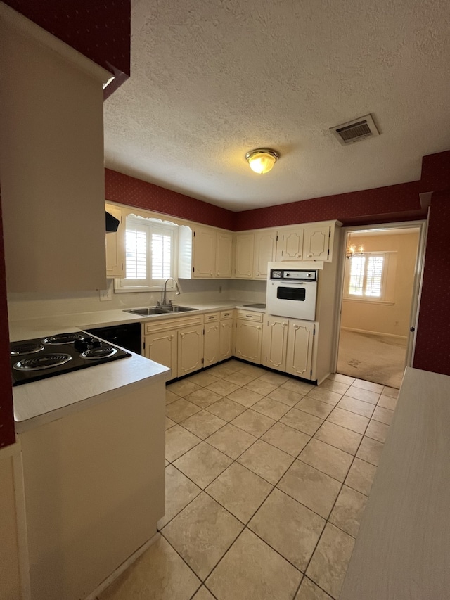 kitchen featuring sink, light tile patterned floors, black electric cooktop, oven, and white cabinets