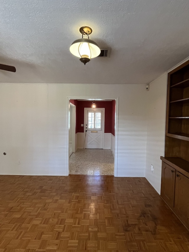 spare room featuring built in features, dark parquet floors, and a textured ceiling