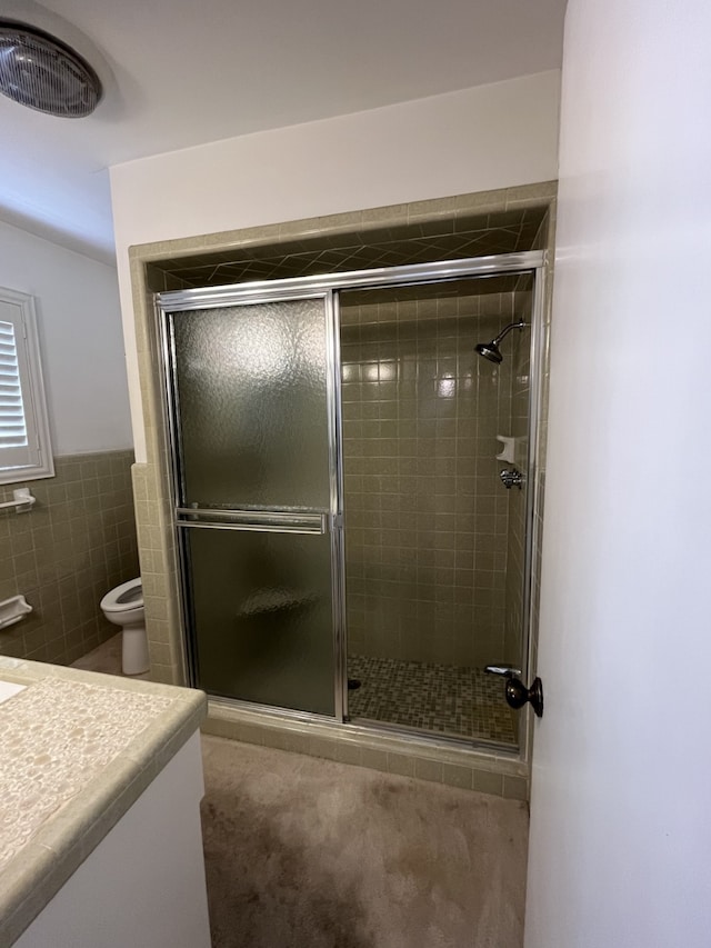 bathroom with vanity, toilet, tile walls, and a shower with shower door