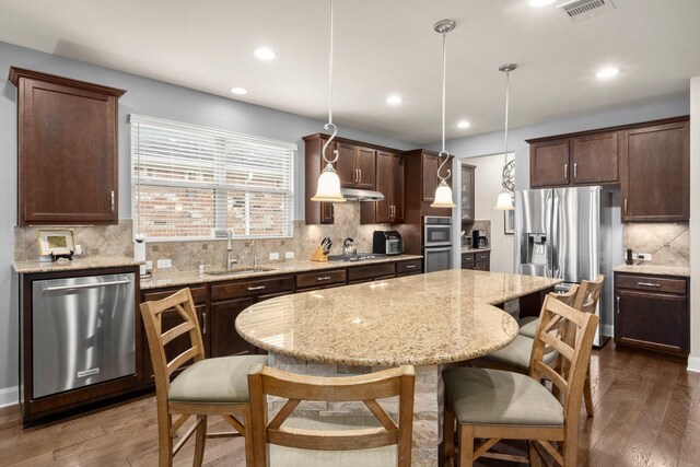 kitchen with decorative light fixtures, stainless steel appliances, dark wood-type flooring, a sink, and a kitchen island