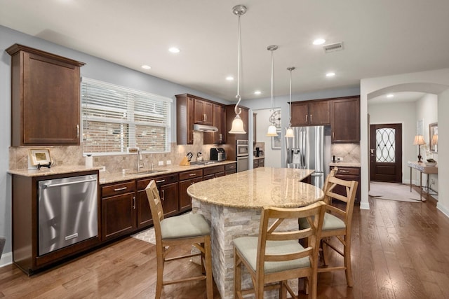 kitchen with arched walkways, stainless steel appliances, a sink, a center island, and pendant lighting