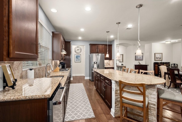 kitchen featuring decorative backsplash, dark wood-style floors, decorative light fixtures, light stone countertops, and stainless steel appliances
