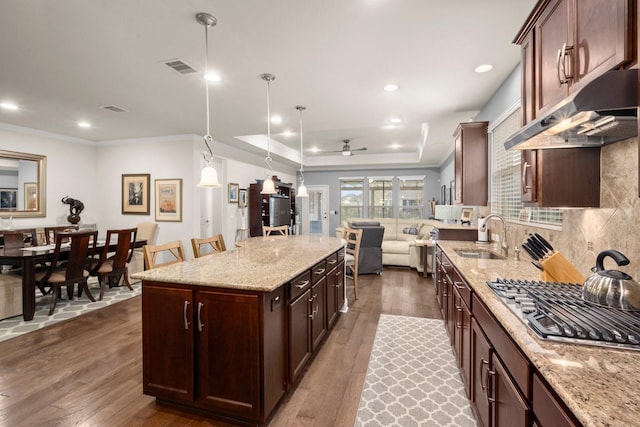 kitchen featuring under cabinet range hood, a sink, open floor plan, hanging light fixtures, and stainless steel gas stovetop