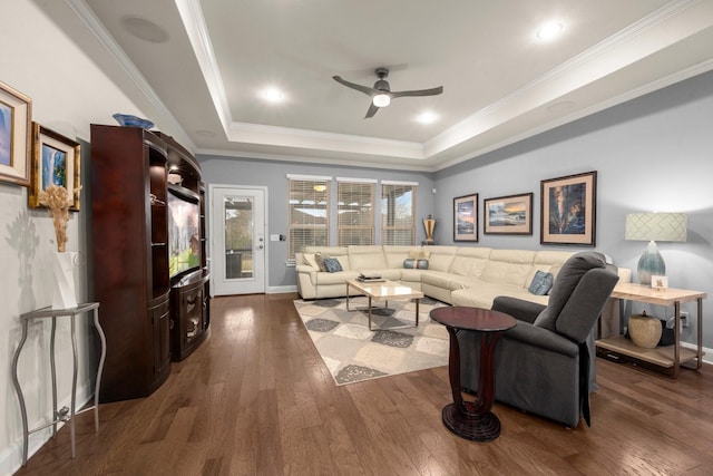 living room with ceiling fan, a tray ceiling, dark wood finished floors, and crown molding