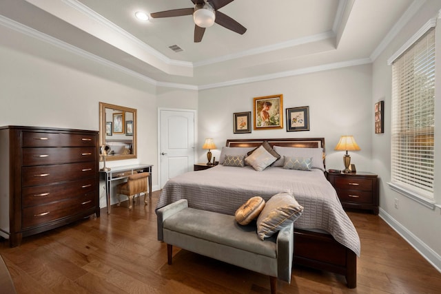 bedroom with ornamental molding, a tray ceiling, dark wood finished floors, and visible vents