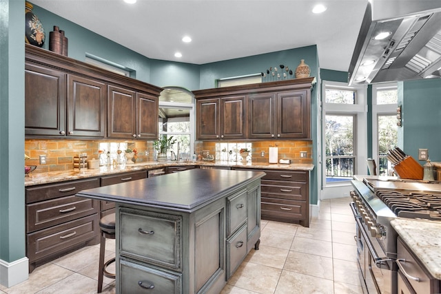 kitchen with a kitchen island, range hood, double oven range, light tile patterned floors, and dark brown cabinetry