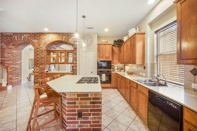 kitchen with sink, hanging light fixtures, a kitchen island, brick wall, and black appliances