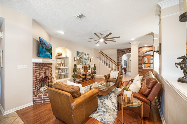 living room with light hardwood / wood-style flooring, ceiling fan, a textured ceiling, a brick fireplace, and built in shelves