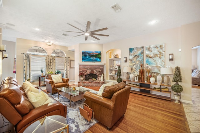 living room with a fireplace, ceiling fan, light hardwood / wood-style floors, a textured ceiling, and built in shelves