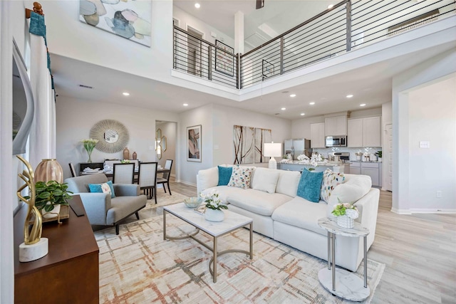 living area with a high ceiling, recessed lighting, baseboards, and light wood finished floors