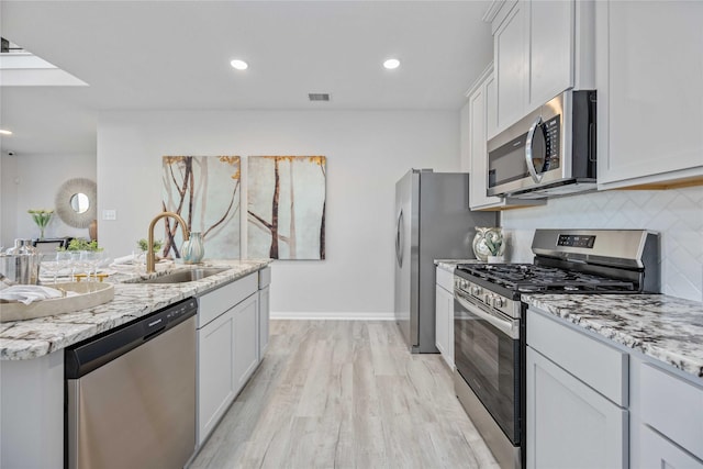 kitchen featuring visible vents, a sink, tasteful backsplash, appliances with stainless steel finishes, and light wood finished floors