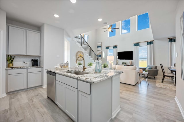 kitchen with light wood-style flooring, a kitchen island with sink, a sink, ceiling fan, and dishwasher