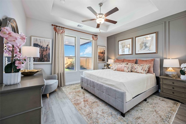 bedroom with visible vents, ceiling fan, baseboards, a tray ceiling, and wood finished floors