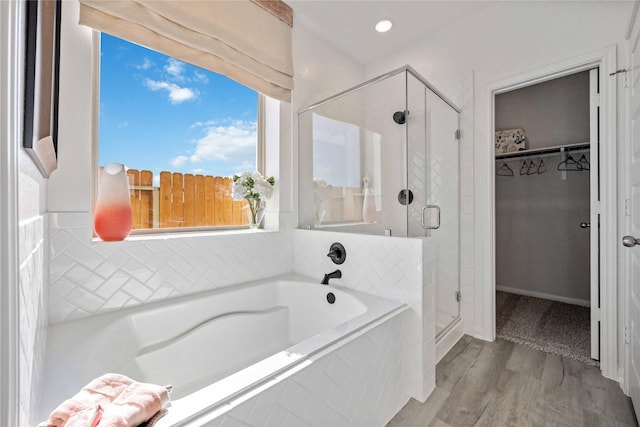 bathroom featuring a spacious closet, a shower stall, a bath, and wood finished floors