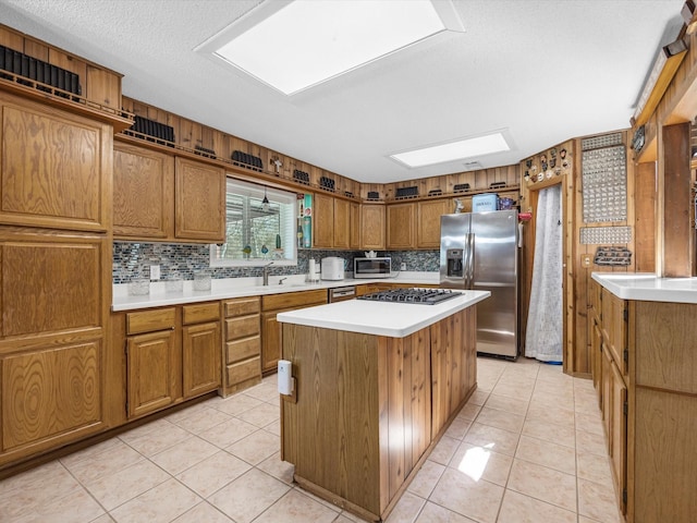 kitchen with appliances with stainless steel finishes, backsplash, a skylight, a center island, and light tile patterned flooring