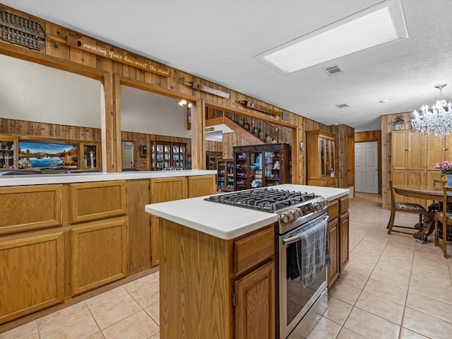 kitchen with light tile patterned flooring, wood walls, a center island, a textured ceiling, and stainless steel range with gas stovetop