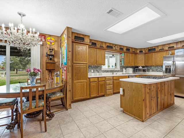 kitchen with a skylight, hanging light fixtures, a kitchen island, stainless steel appliances, and decorative backsplash