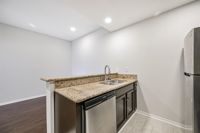 kitchen with sink, light stone countertops, kitchen peninsula, and appliances with stainless steel finishes