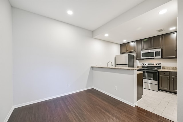 kitchen featuring kitchen peninsula, light stone counters, dark brown cabinetry, stainless steel appliances, and light wood-type flooring