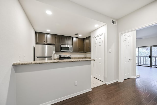 kitchen with appliances with stainless steel finishes, hardwood / wood-style floors, dark brown cabinets, light stone countertops, and kitchen peninsula