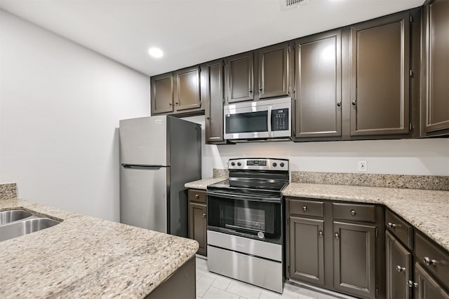 kitchen with stainless steel appliances, sink, light tile patterned floors, and dark brown cabinetry