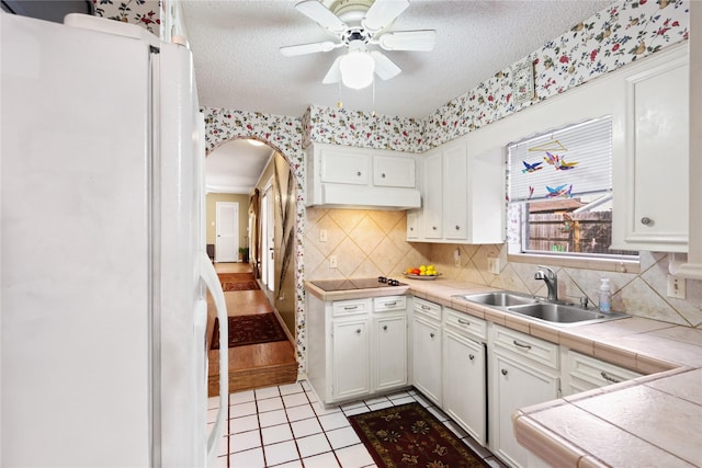 kitchen with tile countertops, white cabinetry, sink, white refrigerator, and a textured ceiling