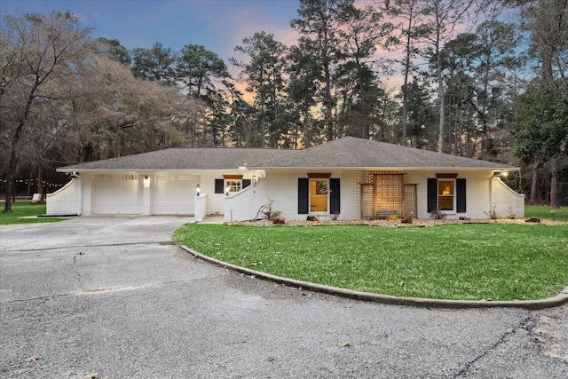 ranch-style house with a garage, brick siding, driveway, roof with shingles, and a front yard