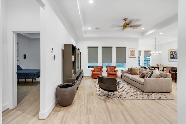 living room with ceiling fan with notable chandelier, a tray ceiling, light hardwood / wood-style floors, and crown molding