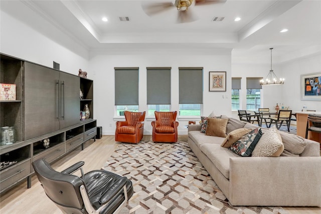 living room with crown molding, light hardwood / wood-style flooring, ceiling fan with notable chandelier, and a tray ceiling