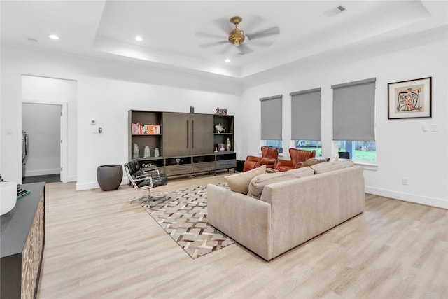 living room with light hardwood / wood-style floors, a raised ceiling, and ceiling fan