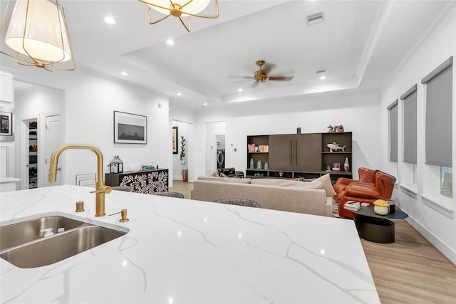 kitchen with pendant lighting, sink, light stone countertops, and a raised ceiling