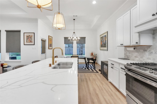 kitchen with decorative light fixtures, stainless steel gas stove, sink, light stone counters, and a raised ceiling