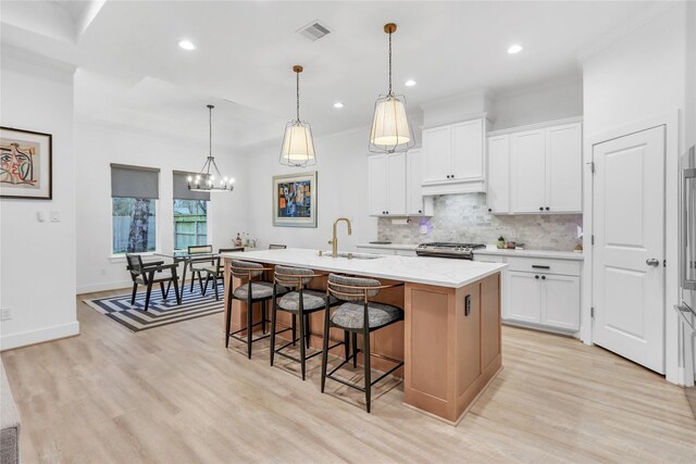 kitchen with sink, stainless steel range, white cabinets, and a center island with sink