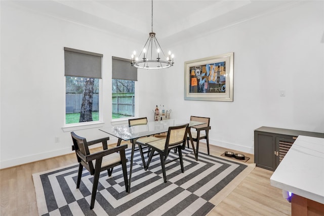 dining room featuring a raised ceiling, ornamental molding, an inviting chandelier, and light hardwood / wood-style flooring