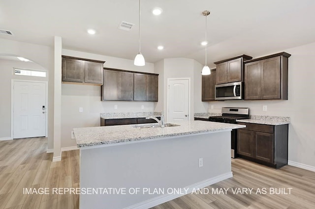 kitchen featuring sink, decorative light fixtures, appliances with stainless steel finishes, light stone countertops, and a kitchen island with sink