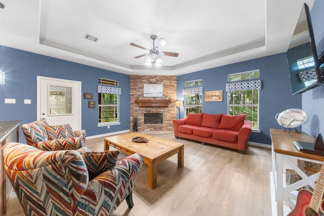 living room with a raised ceiling, ceiling fan, a fireplace, and light hardwood / wood-style flooring