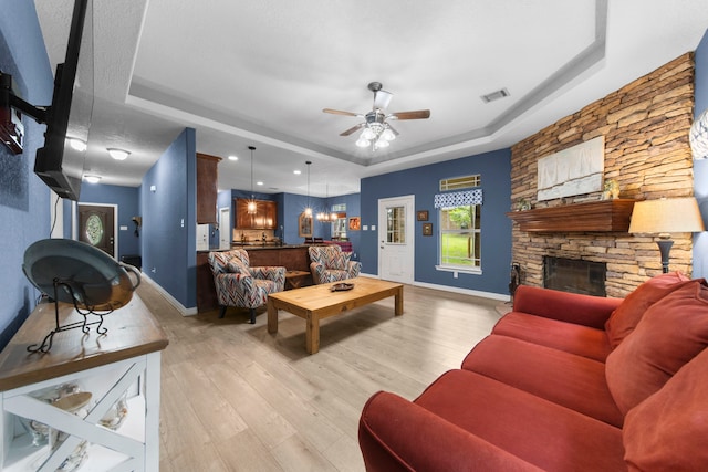 living room featuring a tray ceiling, a fireplace, ceiling fan, and light wood-type flooring