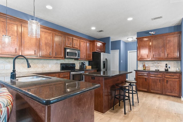 kitchen with sink, appliances with stainless steel finishes, dark stone countertops, a center island, and decorative light fixtures