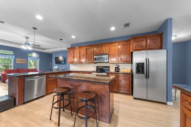 kitchen with a breakfast bar, hanging light fixtures, appliances with stainless steel finishes, kitchen peninsula, and a kitchen island