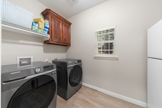 clothes washing area with cabinets, separate washer and dryer, a textured ceiling, and light wood-type flooring