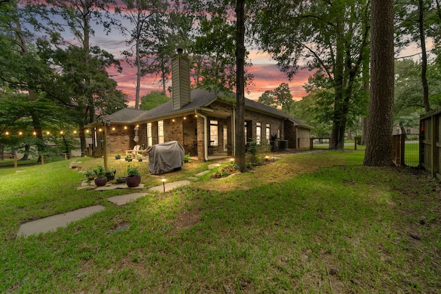 back house at dusk featuring a yard, central AC, and a patio