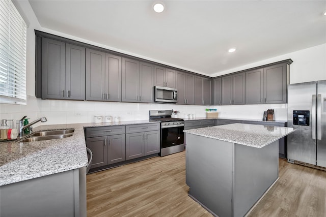 kitchen featuring sink, light hardwood / wood-style flooring, a kitchen island, stainless steel appliances, and light stone countertops