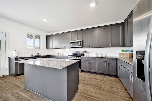 kitchen with light stone counters, appliances with stainless steel finishes, a kitchen island, and light wood-type flooring