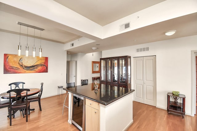 kitchen featuring light hardwood / wood-style flooring, a breakfast bar area, a kitchen island, decorative light fixtures, and beverage cooler